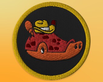 Könnte beinhalten: Ein runder, gelb gerandeter Patch mit schwarzem Hintergrund zeigt eine Cartoon-Illustration einer roten und orangefarbenen Kreatur, die einen gelben Cowboyhut trägt. Die Kreatur hat einen gefleckten Körper und ein breites Lächeln.