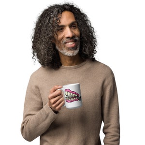 May include: A white coffee mug with a pink and yellow cartoon image of a set of dentures with a gold chain.