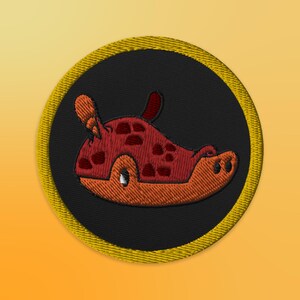 May include: A round embroidered patch with a yellow border and a black background. The patch features a cartoon sea slug with red and orange colors.