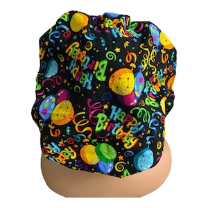 May include: A black scrub hat with a colorful print of balloons, confetti, and the words "Happy Birthday".