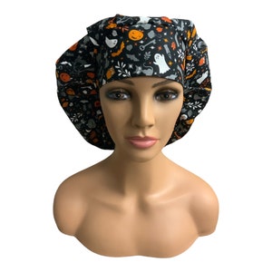 May include: Black scrub hat with a Halloween-themed print featuring ghosts, pumpkins, bats, and other spooky elements. The print is in orange, white, and gray on a black background.