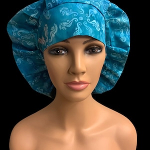 May include: A teal bouffant scrub cap with a seahorse and swirl pattern. The cap is made of fabric and has a wide band around the forehead. The background is black.