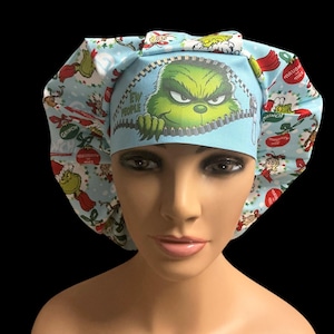 May include: A light blue surgical scrub cap featuring a Grinch design. The cap has a zipper graphic with the Grinch's face peeking out, and the text "EW PEOPLE". The cap is patterned with Grinch characters and Christmas elements.