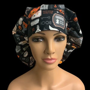 May include: Black Halloween-themed bouffant scrub cap. The cap features a repeating pattern of ghosts, pumpkins, and potion bottles. Text includes "BOO!", "GHOSTS have the real spirit", and "31".