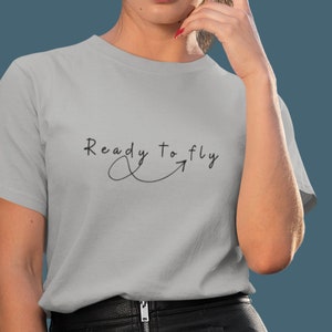 May include: A grey t-shirt with the text "Ready to fly" written in black cursive with an arrow pointing to the right.