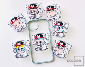 May include: A selection of clear phone grip stickers depicting cartoon characters in white bunny costumes with red and black hats. The stickers are arranged around a clear phone case with a pale blue edge. The stickers show various expressions.