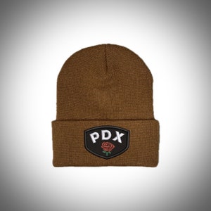 May include: A brown knit beanie with a black patch featuring a white "PDX" and a red rose.