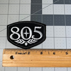 May include: Black and white embroidered patch with the number 805 and a star in the center. The patch is shaped like a shield with a white laurel wreath at the bottom.