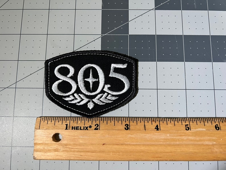 May include: Black and white embroidered patch with the number 805 and a star in the center. The patch is shaped like a shield with a white laurel wreath at the bottom.