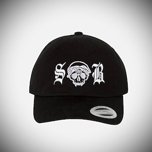 May include: Black baseball cap with a white embroidered skull and the letters "SOR" in a gothic font.
