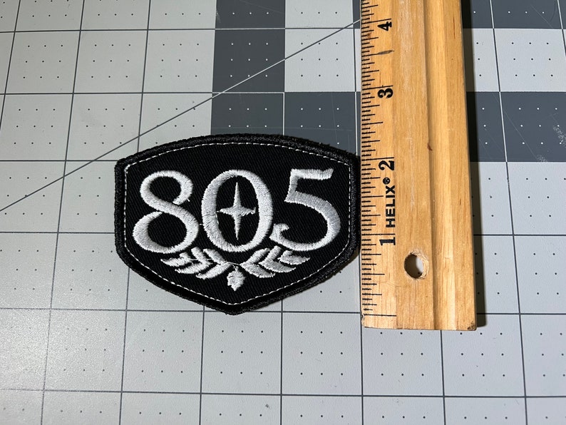 May include: Black and white embroidered patch with the number 805 and a star in the center. The patch is shaped like a shield and has a white embroidered design around the number.