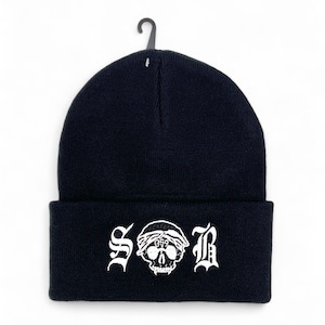 May include: Black beanie with white embroidered design. The design features the letters "S O B" with a skull wearing a bandana in the center. The beanie is hanging from a black plastic hook.