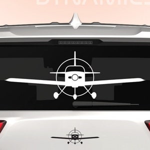 May include: White car with a Dingo Dynamics logo and a white silhouette of a small plane on the back window. The plane has a propeller and landing gear.