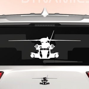 May include: White silhouette of a helicopter on the rear window of a white SUV. The SUV has a DINGO logo on the rear bumper and a blue and white American flag sticker on the lower right side of the bumper.
