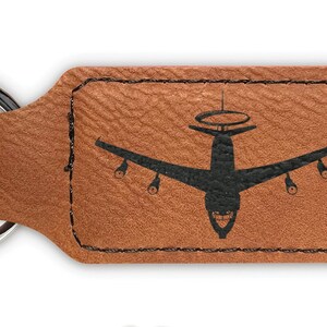 May include: A brown leather keychain with a silver key ring. The keychain features a black silhouette of a B-52 bomber airplane. The text "DINGO DYNAMICS" is visible in the lower right corner of the image.