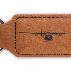May include: Brown leather keychain with a silver key ring. The keychain features a silhouette of a small airplane.