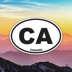Peut inclure: Un autocollant ovale avec une bordure blanche présente les lettres noires en gras "CA" au-dessus du mot "CANADA". L'autocollant est placé sur un fond de chaîne de montagnes sous un ciel coloré.