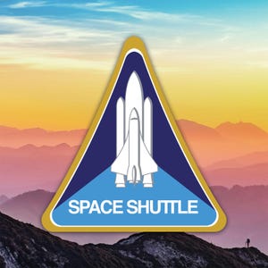 May include: A triangular patch featuring a white space shuttle design on a blue background, with the words "SPACE SHUTTLE" in white. The patch has a gold border and is set against a scenic mountain backdrop with a colorful sky.