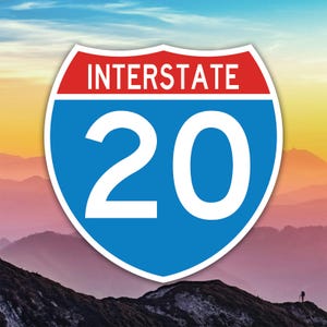 May include: A road sign for Interstate 20, featuring a blue shield with the number 20 in white, and the word "INTERSTATE" in white on a red banner. The sign is set against a scenic background of mountains and a colorful sky.
