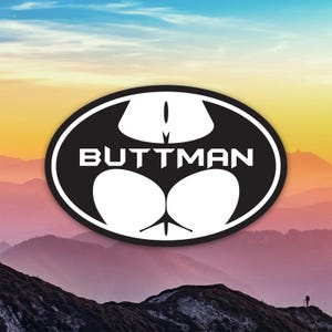 May include: A black and white oval sticker with the text "BUTTMAN" in a bold font. The design features a stylized image of a butt, with a bat-like shape above. The background shows a mountain range under a colorful sky.