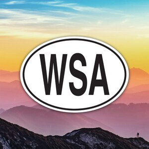May include: An oval sticker with the letters "WSA" in bold black font, set against a white background. The sticker is placed over a scenic background of layered mountain ranges under a colorful sky.