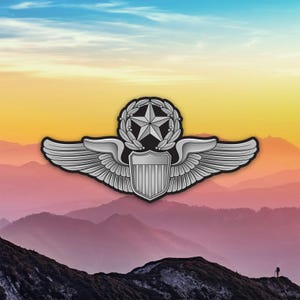 May include: A silver-colored pilot's badge with a star, laurel wreath, and wings. The badge features a shield design at the bottom. The background shows a mountain range with a colorful sky.