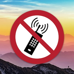 Puede incluir: Un letrero redondo rojo con un centro blanco que presenta un teléfono móvil negro con ondas de señal, tachado con una línea diagonal roja. El fondo muestra una cordillera bajo un cielo colorido.