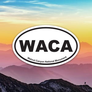 May include: An oval sticker featuring the letters "WACA" in bold black lettering. The text "Walnut Canyon National Monument" is below. The sticker is set against a backdrop of mountains and a colourful sky.