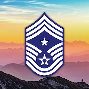 May include: A blue and white military insignia, with a star and stripes design. The emblem is set against a scenic backdrop of mountains and a colourful sky, suggesting a badge or patch.