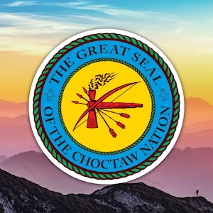 May include: A circular emblem featuring the text "THE GREAT SEAL OF THE CHOCTAW NATION" in a blue ring. The emblem's center is yellow, with a red bow and arrows, and a smoking pipe. The background shows a mountain range.
