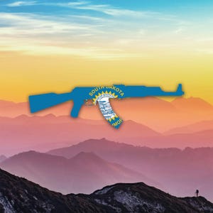May include: A blue silhouette of an AK-47 rifle overlaid with the South Dakota state flag. The image is set against a backdrop of layered purple mountains and a colourful sunset.