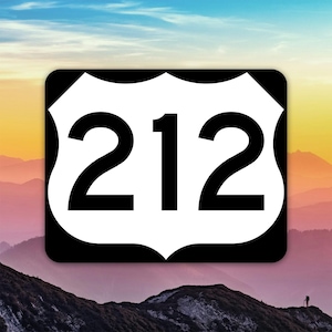 以下が含まれることがあります： 白と黒のUS Route 212の道路標識。標識は黒い縁取りと、太字の黒いフォントで数字212を表示しています。背景には、山々と色鮮やかな空の美しい景色が広がっています。