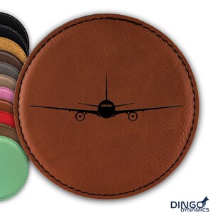 May include: A brown leather coaster with a black silhouette of an airplane in the center.