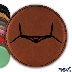 May include: A brown leather coaster with a black silhouette of a V-22 Osprey aircraft.