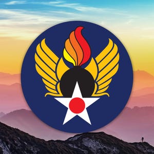 May include: A circular emblem featuring a white star with a red center, set against a dark blue background. Above the star is a black shape with yellow wings and a flame in red, orange, and yellow. The emblem is set against a mountain landscape.