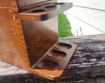 May include: A vintage wooden pipe stand with a dark stain. The stand has two levels with circular and oval cutouts to hold pipes. The wood grain is visible, and the stand appears to be well-crafted.