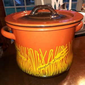 Könnte beinhalten: Orangener Keramiktopf mit braunem Deckel und gelbem Spaghetti-Design. Der Topf trägt die Aufschrift "Spaghetti al ragu".
