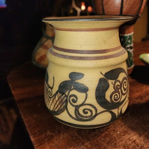 Może przedstawiać: Mały, brązowy ceramiczny wazon z czarnym i brązowym wzorem kwiatowym. Wazon ma szeroki otwór i zaokrąglone ciało.