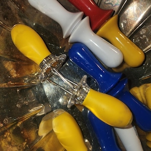May include: A set of five colorful kitchen tools with yellow, blue, white, and red handles. The tools have a silver metal base and are designed for serving food.