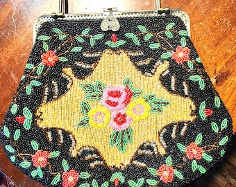 May include: A vintage beaded purse with a black background and a floral design in shades of pink, yellow, green, and red. The purse has a metal frame and a top handle.