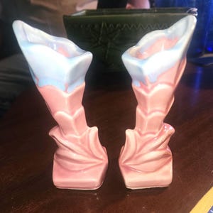 Puede incluir: Un par de jarrones de cerámica rosa y azul con un diseño floral. Los jarrones tienen la forma de una flor de trompeta.