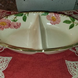 May include: Oval-shaped divided serving dish with a cream-colored interior and a gold rim. The dish is decorated with pink and yellow roses and green leaves. A vintage piece for serving snacks or appetizers.