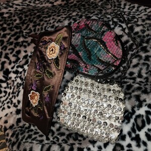 May include: Three different purses, one brown with floral embroidery, one white with silver sequins, and one round with a pink and green sequined design.