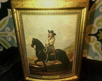 May include: A gold-colored ceramic decanter with a vintage-style image of a man on a horse. The image is framed with a gold border and the text "Man on a Horse by Geyer" is printed below the image.