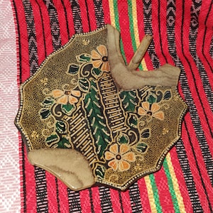 Pode incluir: Um prato octogonal decorativo com um design floral castanho e dourado, com detalhes em laranja e verde. Duas formas abstratas bege estão presas ao prato. O prato repousa sobre um tecido listrado vermelho e preto.
