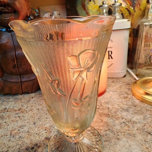 May include: A clear glass vase with a fluted design and a floral pattern. The vase has a wide mouth and a narrow base.