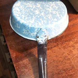 Könnte beinhalten: Ein blauer und weißer Emaille-Topf mit einem schwarzen Griff. Der Topf hat ein gesprenkeltes Muster.