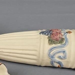 Puede incluir: Jarrón de cerámica color crema con diseño acanalado vertical. Decorado con una rosa rosa, una cinta azul y uvas moradas. El jarrón tiene un borde acampanado y un extremo verde. Mide unos 25 cm de largo.