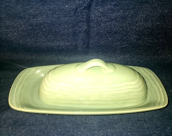 May include: A green ceramic butter dish with a lid and a handle. The dish has a wavy design.