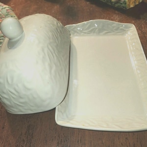 May include: White ceramic butter dish with a domed lid and a rectangular tray. The lid has a textured design and a knob on top. The tray has a raised edge and a textured design.